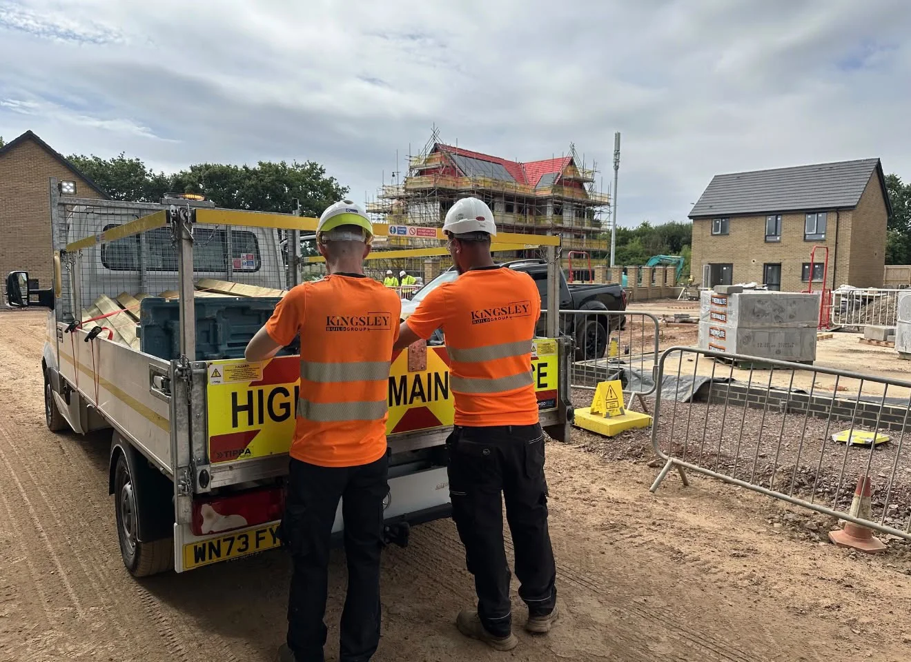 Two Kingsley operatives in Kingsley hi-vis and hard hats beside a highway maintenance truck on a housing site