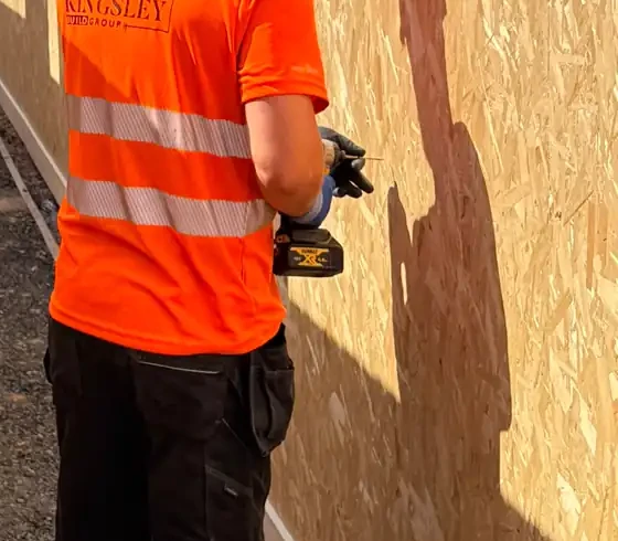 Kingsley operative in Kingsley hi-vis drilling OSB hoarding along a site boundary