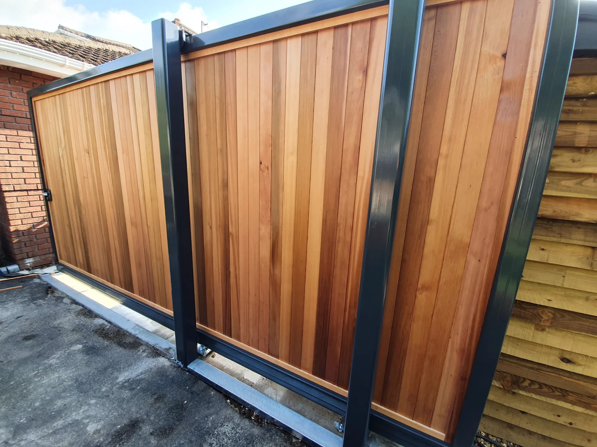 Cedar-boarded sliding gate in an anthracite steel frame, by Kingsley Build Group