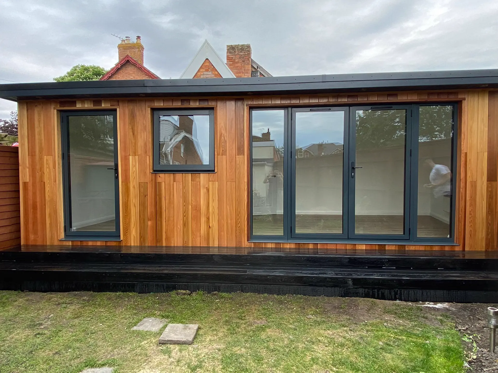 Cedar-clad garden room with grey bi-fold doors and a dark deck, by Kingsley Build Group